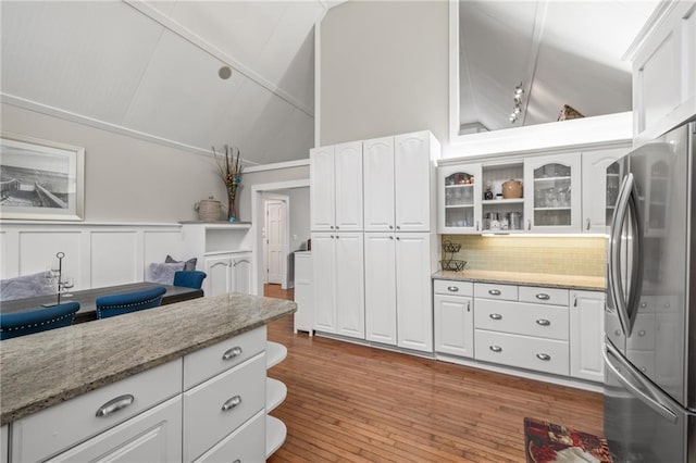 kitchen with tasteful backsplash, light stone counters, light hardwood / wood-style flooring, white cabinets, and stainless steel refrigerator