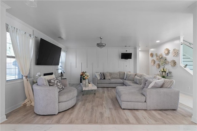 living room with a large fireplace, light hardwood / wood-style floors, and crown molding