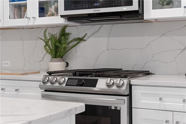 kitchen featuring light stone counters, tasteful backsplash, gas stove, range hood, and white cabinets