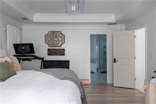 bedroom featuring connected bathroom, a raised ceiling, hardwood / wood-style flooring, and crown molding