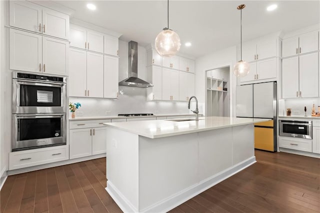 kitchen featuring refrigerator, wall chimney range hood, light countertops, double oven, and a sink