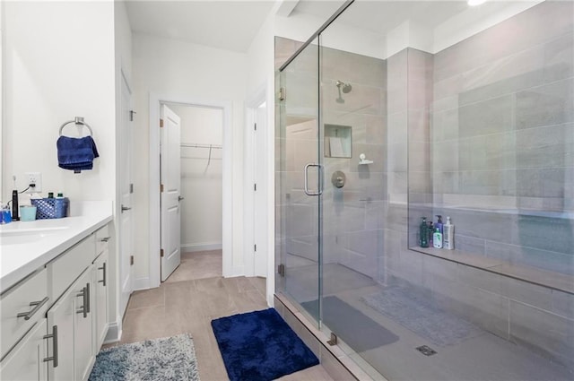 bathroom with a shower stall, vanity, baseboards, and a spacious closet