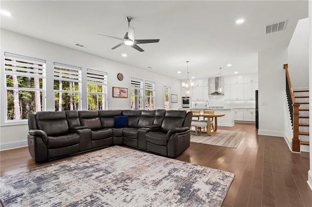 living room with stairs, visible vents, ceiling fan with notable chandelier, and dark wood finished floors