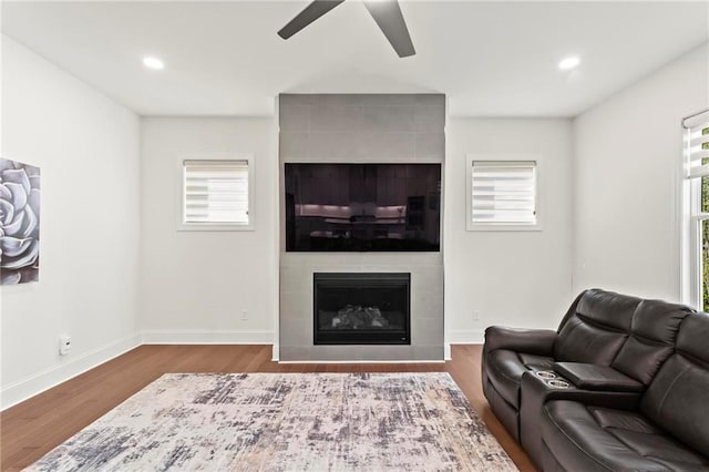 living area featuring baseboards, recessed lighting, a fireplace, a ceiling fan, and wood finished floors