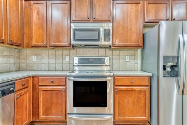 kitchen with decorative backsplash, light countertops, brown cabinetry, and appliances with stainless steel finishes