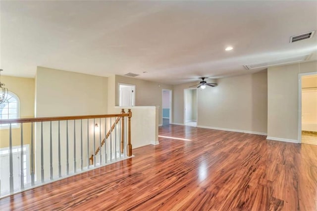 empty room with visible vents, attic access, wood finished floors, and ceiling fan with notable chandelier