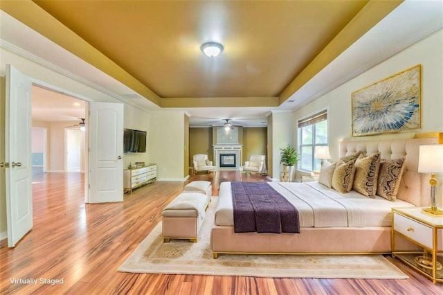 bedroom with a glass covered fireplace, a tray ceiling, baseboards, and wood finished floors