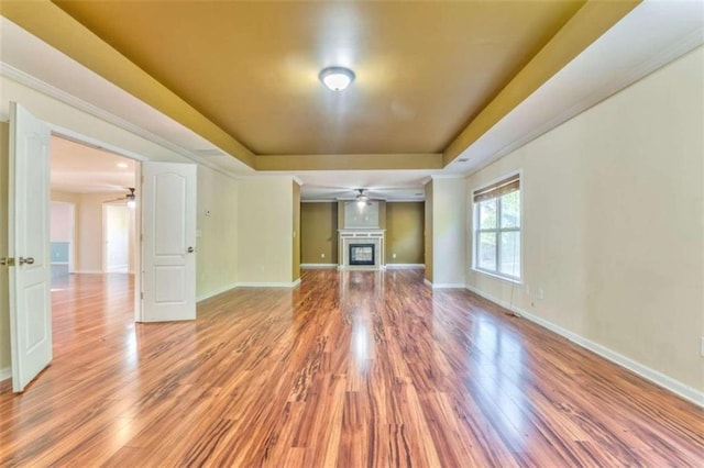 unfurnished living room featuring baseboards, a raised ceiling, light wood-style floors, and a ceiling fan