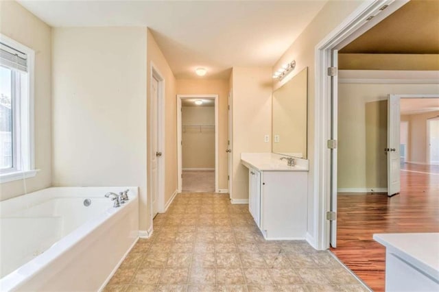 bathroom with vanity, a garden tub, a spacious closet, and baseboards