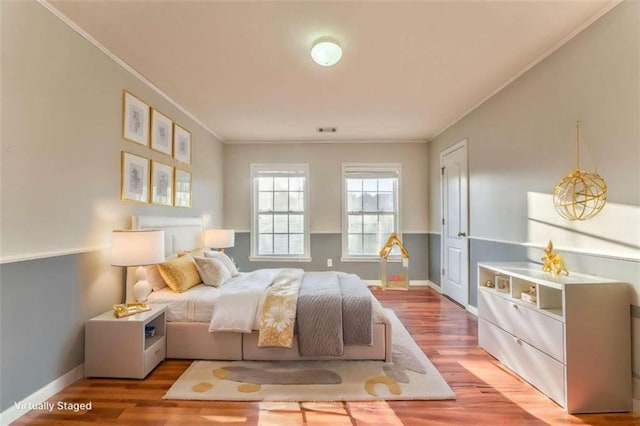 bedroom featuring visible vents, wood finished floors, baseboards, and ornamental molding