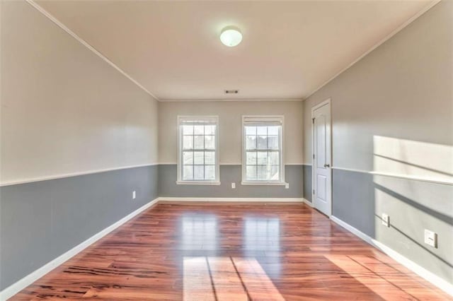 spare room with visible vents, ornamental molding, baseboards, and wood finished floors