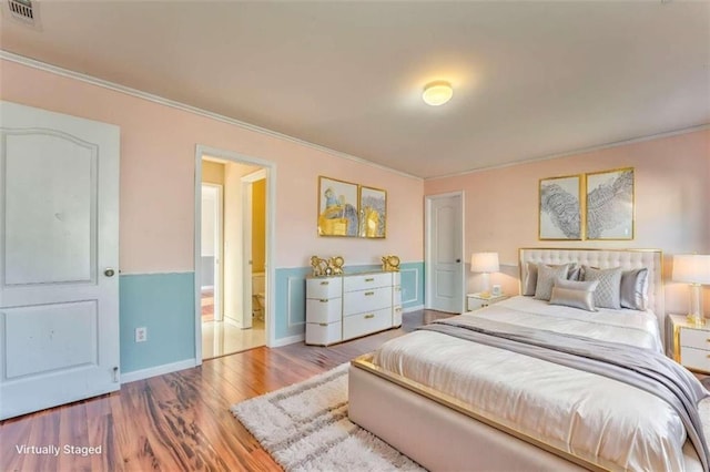 bedroom featuring visible vents, baseboards, wood finished floors, and crown molding