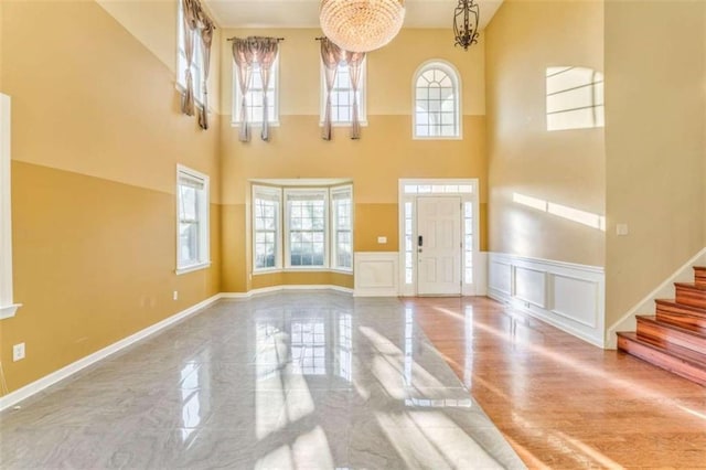 foyer entrance featuring a wainscoted wall, marble finish floor, stairway, a decorative wall, and a towering ceiling