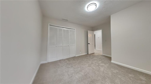 unfurnished bedroom featuring baseboards, visible vents, a textured ceiling, carpet floors, and a closet