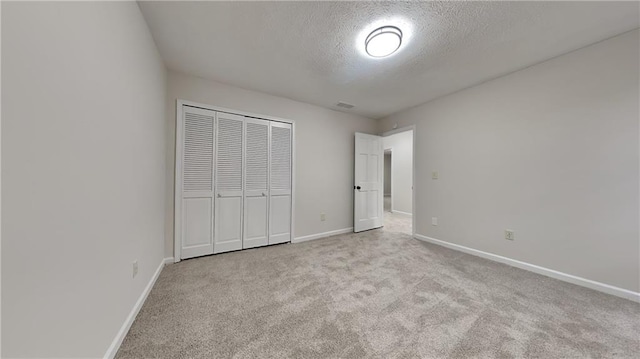 unfurnished bedroom with visible vents, baseboards, a textured ceiling, carpet floors, and a closet