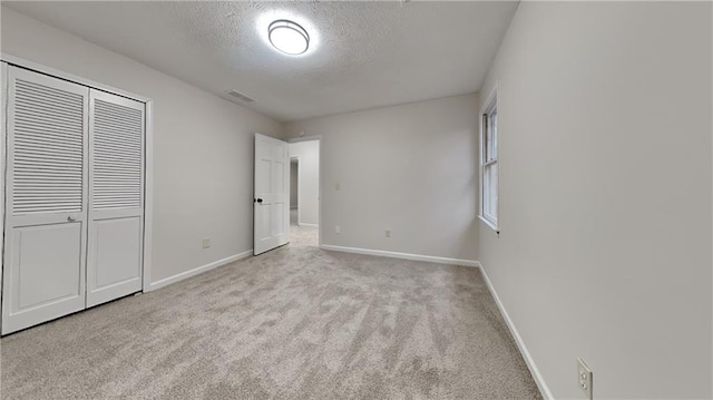 unfurnished bedroom with a textured ceiling, visible vents, baseboards, a closet, and carpet