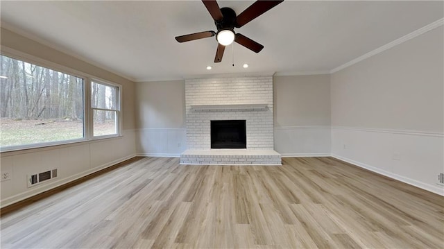 unfurnished living room featuring visible vents, wainscoting, ornamental molding, wood finished floors, and a fireplace