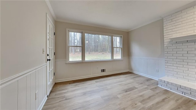 empty room featuring ornamental molding, wainscoting, wood finished floors, and visible vents