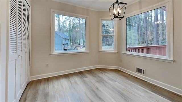 unfurnished dining area featuring baseboards, visible vents, wood finished floors, crown molding, and a chandelier