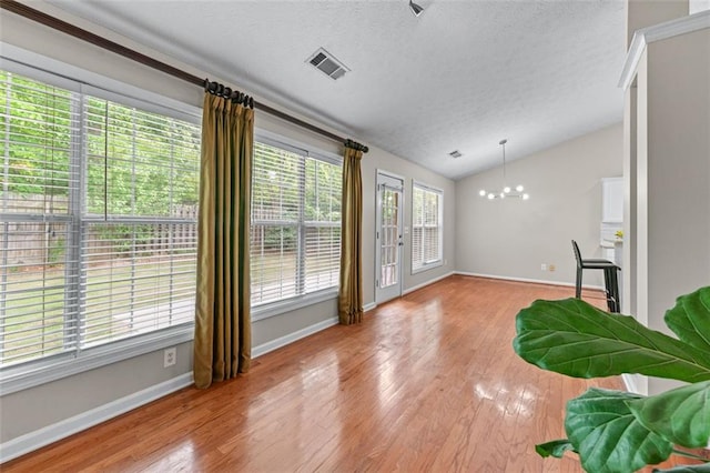 living area with lofted ceiling, a chandelier, light wood-style floors, a textured ceiling, and baseboards