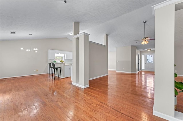 unfurnished living room featuring lofted ceiling, light wood-type flooring, ceiling fan, baseboards, and a chandelier
