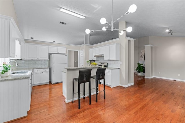 kitchen featuring freestanding refrigerator, a sink, backsplash, white cabinetry, and a kitchen island