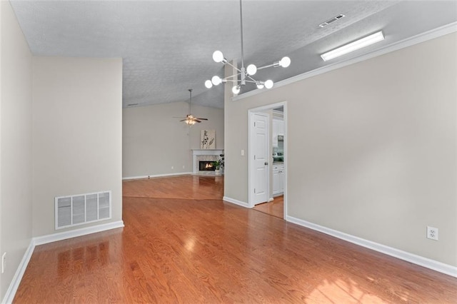 spare room with wood finished floors, a chandelier, vaulted ceiling, a fireplace with flush hearth, and ceiling fan