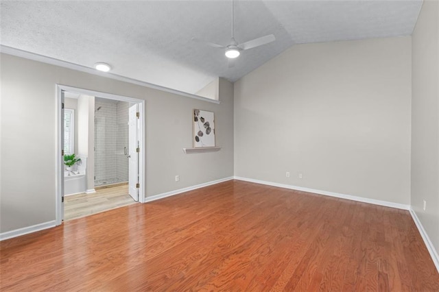 spare room featuring a ceiling fan, wood finished floors, baseboards, vaulted ceiling, and a textured ceiling