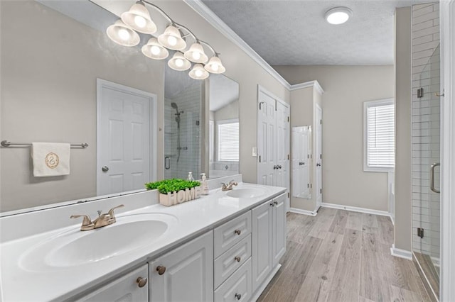 full bath with a shower stall, healthy amount of natural light, double vanity, wood finished floors, and a textured ceiling