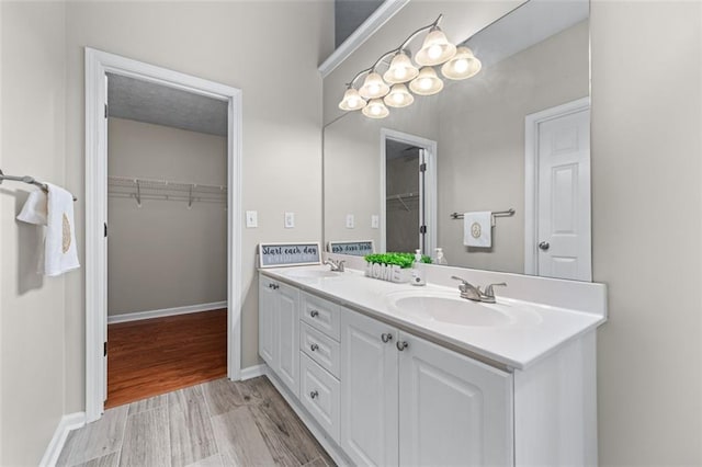 bathroom featuring double vanity, a spacious closet, wood finished floors, and baseboards