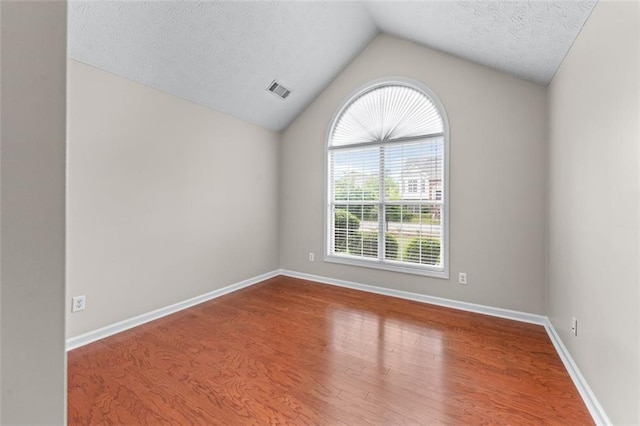 empty room featuring wood finished floors, lofted ceiling, a textured ceiling, and baseboards