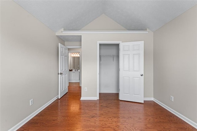 unfurnished bedroom with wood finished floors, vaulted ceiling, a closet, a textured ceiling, and baseboards