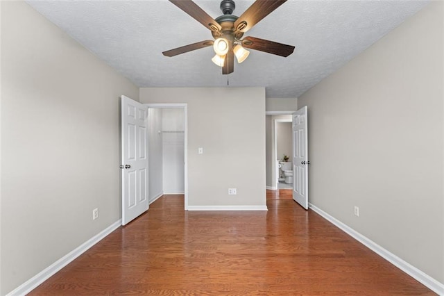unfurnished bedroom with wood finished floors, baseboards, a walk in closet, a textured ceiling, and a closet