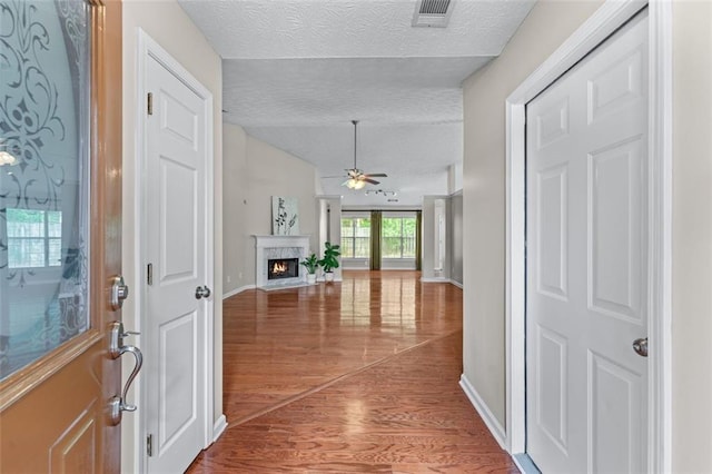 entrance foyer featuring a textured ceiling, wood finished floors, ceiling fan, baseboards, and a warm lit fireplace