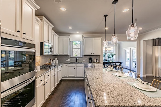 kitchen featuring backsplash, dark wood-type flooring, appliances with stainless steel finishes, pendant lighting, and ornamental molding