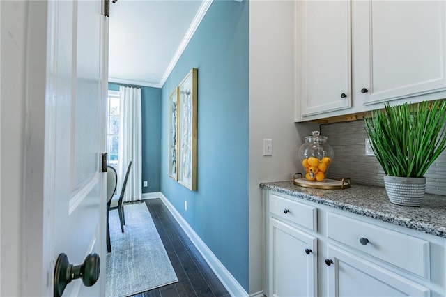 bar featuring dark hardwood / wood-style flooring, tasteful backsplash, white cabinets, light stone countertops, and ornamental molding