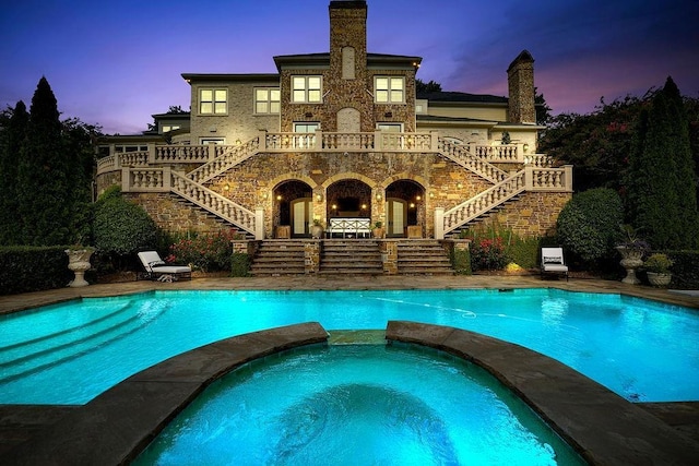 back house at dusk with a swimming pool with hot tub