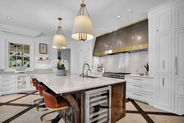 kitchen with an island with sink, decorative light fixtures, beverage cooler, white cabinetry, and backsplash