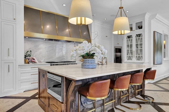 kitchen with hanging light fixtures, backsplash, a kitchen bar, a center island with sink, and white cabinets