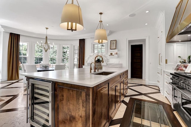 kitchen featuring a chandelier, beverage cooler, a center island with sink, range with two ovens, and sink