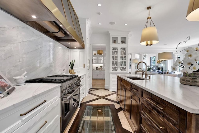 kitchen featuring hanging light fixtures, tasteful backsplash, wall chimney range hood, sink, and range with two ovens