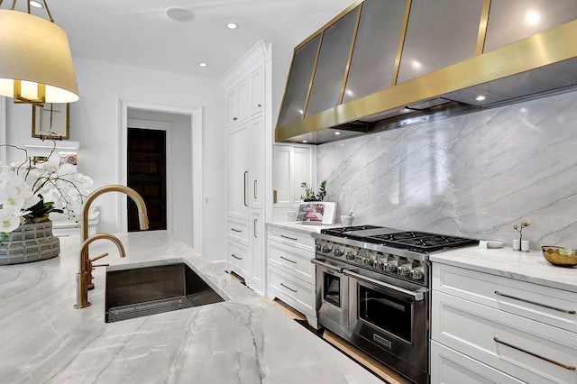 kitchen with light stone counters, tasteful backsplash, white cabinetry, double oven range, and wall chimney exhaust hood