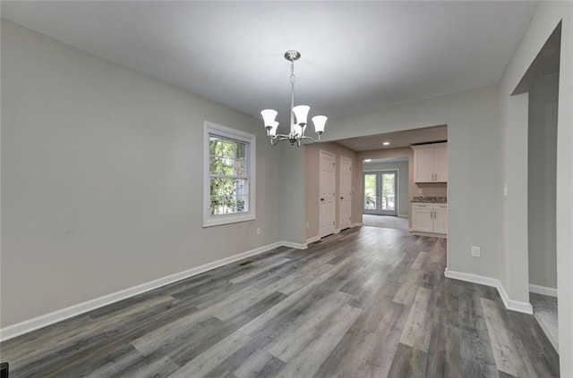 unfurnished dining area with a chandelier, healthy amount of natural light, dark wood finished floors, baseboards, and recessed lighting