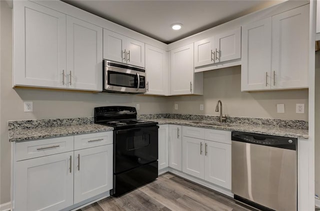 kitchen with appliances with stainless steel finishes, a sink, light wood-style flooring, white cabinetry, and recessed lighting