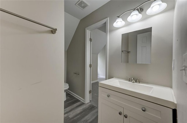bathroom with toilet, vanity, wood finished floors, and baseboards