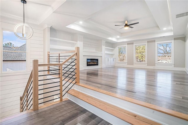 living room with a raised ceiling, visible vents, dark wood-type flooring, a glass covered fireplace, and ceiling fan