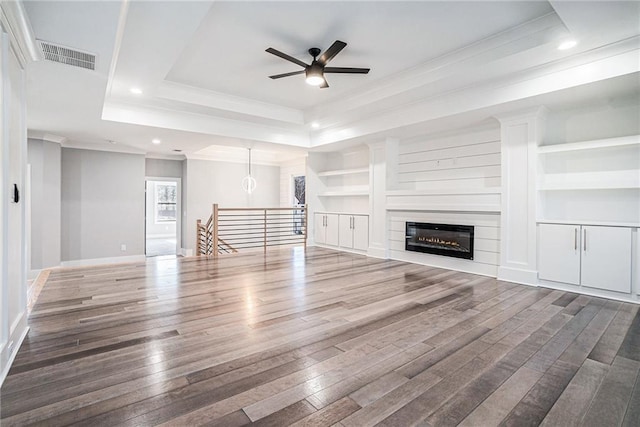 unfurnished living room featuring wood finished floors, visible vents, built in features, a raised ceiling, and crown molding