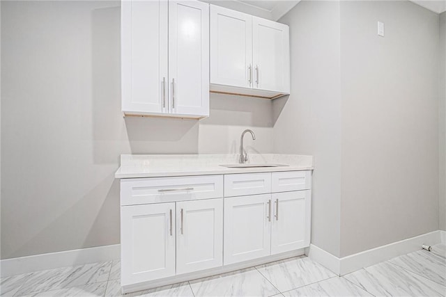 bar featuring marble finish floor, a sink, and baseboards
