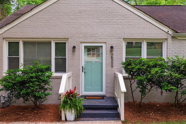 property entrance featuring brick siding and roof with shingles