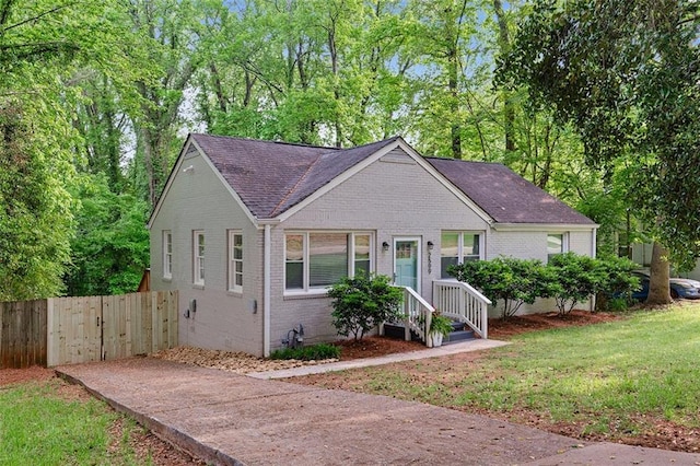 bungalow-style house featuring a front lawn, fence, roof with shingles, and brick siding